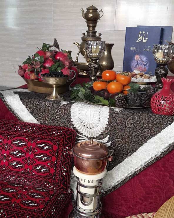 چیدمان سنتی مخصوص شب یلدا با ترکیب کرسی، چراغ گرسوز، پشتی، سماور زغالی، کتاب دیوان حافظ، خرمالو و انار
